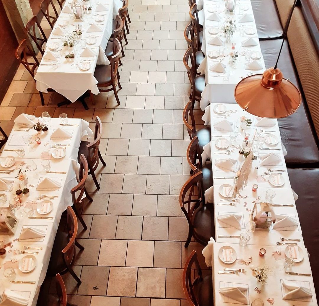 High-angle view of the private dining room set for a banquet — long tables in white linens, glasses and warm pendant light